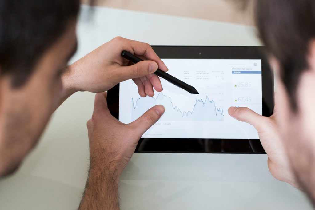 Two analysts comparing stock chart data on tablet discussing analytics discrepancy